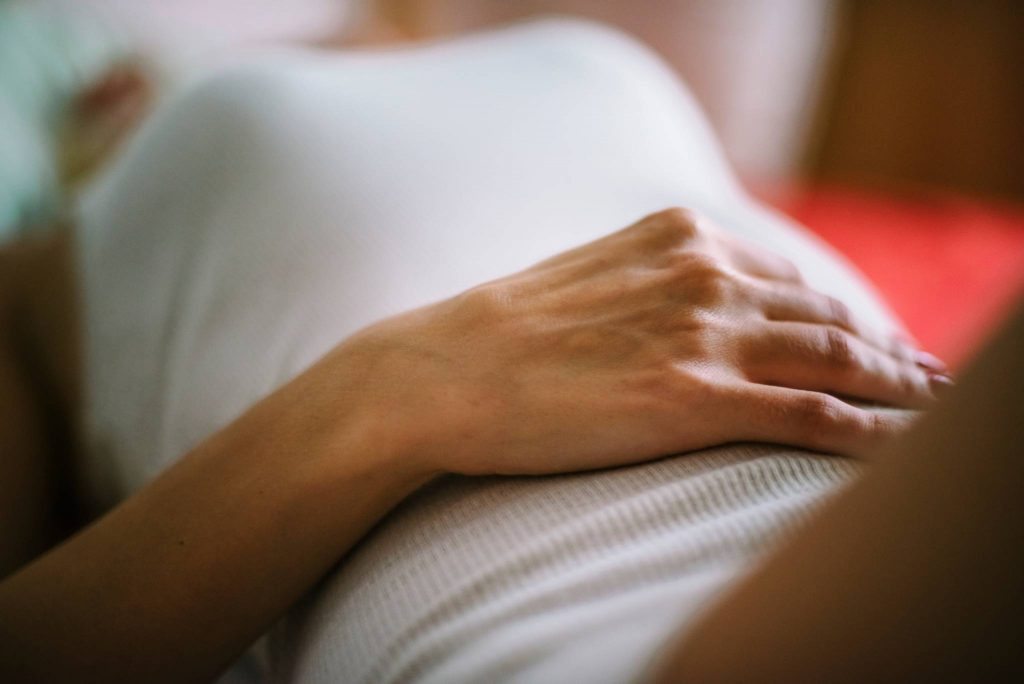 Image of a woman in a white vest lying on her back with her hand resting on her stomach