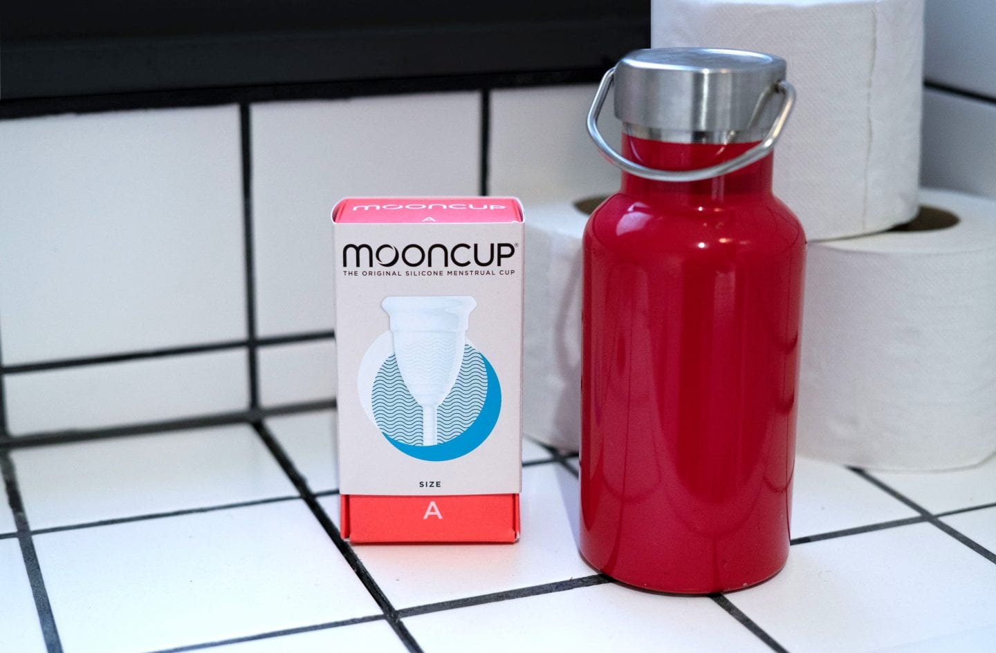 Mooncup in a public toilet next to a red reusable water bottle