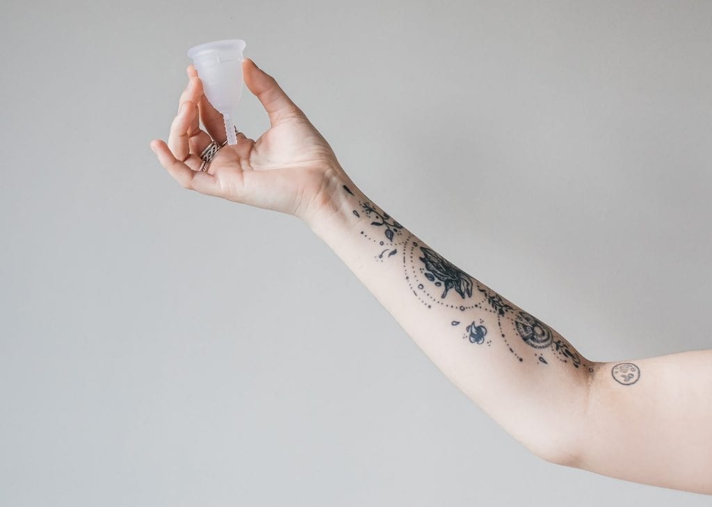 Mooncup menstrual cup held by a tattooed hand