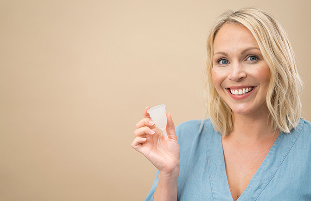 woman smiling and holding a mooncup menstrual cup